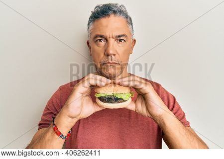 Handsome middle age mature man eating a tasty classic burger relaxed with serious expression on face. simple and natural looking at the camera. 