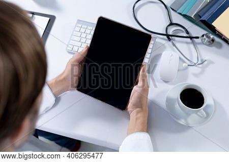Over shoulder view of caucasian male doctor making consultation video call using tablet. telemedicine online healthcare during quarantine lockdown.