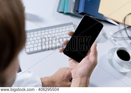 Over shoulder view of caucasian male doctor making consultation video call using smartphone. telemedicine online healthcare during quarantine lockdown.
