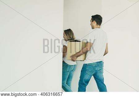 Back View Of Family Holding Boxes During Removal And Going Away From Empty Room. Middle-aged Man And