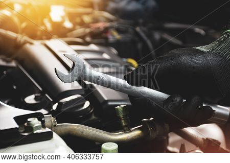 The Mechanic Hand Wearing Black Gloves Holding Open-end Wrench With A Sunlight And Engine Blurred On