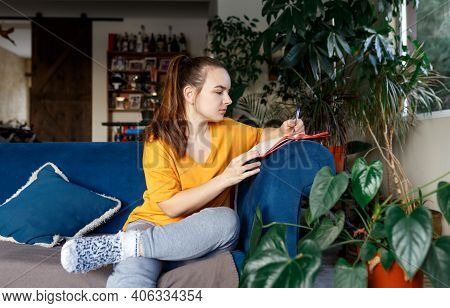 Satisfied And Happy Smiling Girl Sitting On The Sofa In The Room And Writes A Journal Of Your Dreams