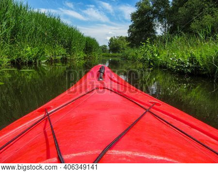 Red Tourist Kayak. Peddeling On A Calm River With Green Plants And Grass