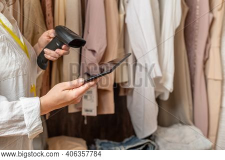A Warehouse Woman Employee Accepts Clothes Using Tablet, Barcode Scanner Reading A Bar Code From Pri
