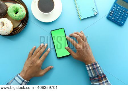 Top View Of Man Hand Using Smart Phone With Donuts, Tea Blue Background
