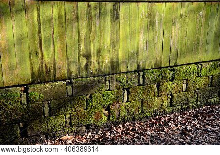 Mossy And Lichen-covered Wall Fences And Wooden Planks. The Blocks Of The Foundation Resemble The Ma