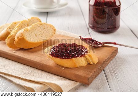 Tasty Sandwich With Raspberry Jam, Few Baguette Slices And Spoon On A Wood Cutting Board Against Jam