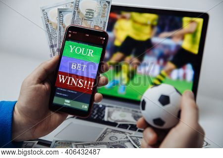 Smartphone With Betting Mobile Application And Males Hand With Soccer Ball. Sport And Betting Concep