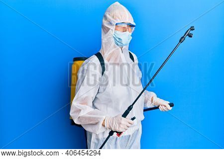 Covid specialist wearing decontamination protective suit and disinfectant spray, decontaminate and sanitize surface, standing over blue background