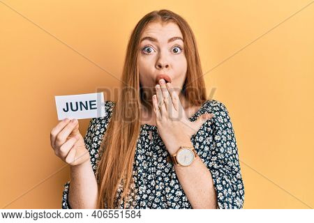 Young beautiful redhead woman holding june word on paper covering mouth with hand, shocked and afraid for mistake. surprised expression 
