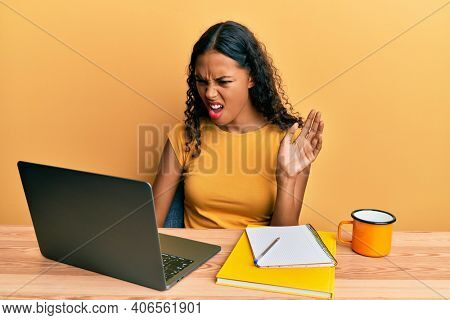 Young african american girl doing video call waving to laptop angry and mad screaming frustrated and furious, shouting with anger. rage and aggressive concept. 