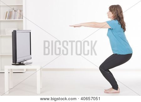 Mulher fazendo fitness em casa usando instruções de TV de tela