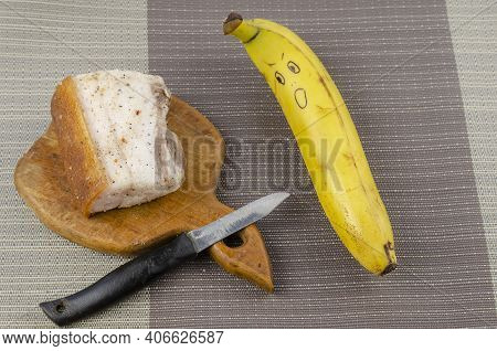 Banana With A Face And A Piece Of Salted Fat With Spices. Ripe Banana With A Grimace Of Surprise. Sa