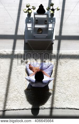 Man Buddhist In White Dress Sitting And Doing Meditation In Front Of Set Of Altar Table With Buddha 