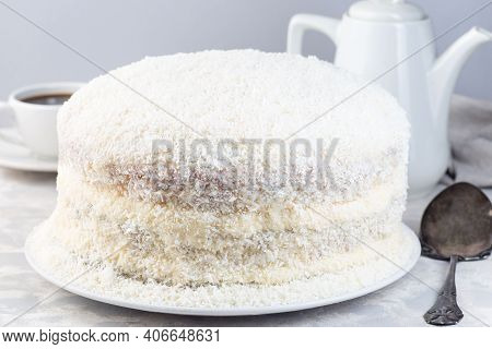 Homemade Coconut Cake With Cream Cheese Frosting And Coconut Flakes Decoration, On A White Plate, Ho