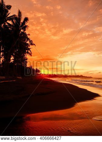 Warm Sunset Or Sunrise With Ocean Waves And Palms At Black Sand Beach In Bali