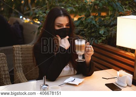 Young Brunette Woman In Medical Mask Drinkingcoffee Latte In Cafe