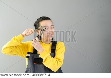 Female Construction Worker Dressed In Special Clothes With A Cordless Screwgun, A Construction Tool 