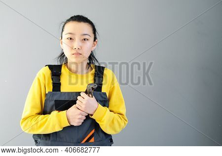 Female Construction Worker Dressed In Special Clothes With A Cordless Screwgun, A Construction Tool 