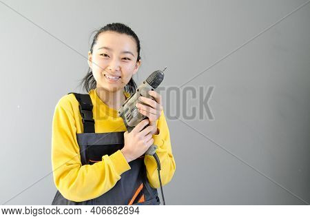 Female Construction Worker Dressed In Special Clothes With A Cordless Screwgun, A Construction Tool 