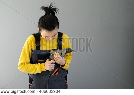 Female Construction Worker Dressed In Special Clothes With A Cordless Screwgun, A Construction Tool 