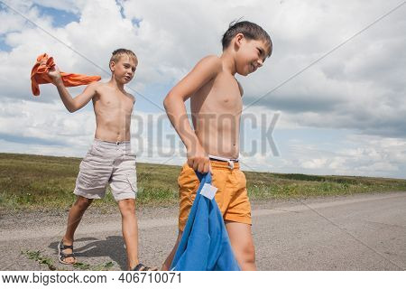 Two Boys In Shorts Cross The Road In The Countryside.