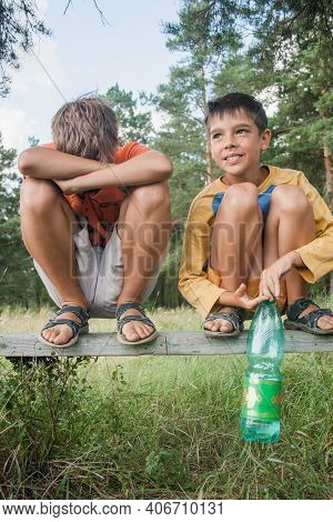 Two Boys In Shorts Sit On A Bench Under A Tree. Boy Looks To The Sky. Dreamer Guy