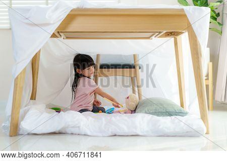 Asian Cute Little Girl Play Cooking And Feeding Food To Her Doll While Sitting In A Blanket Fort In 