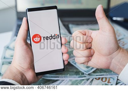 Russia Moscow 02.02.21 Mobile Phone With Logo Of Reddit Traders, Money,dollars In Hands.community Of