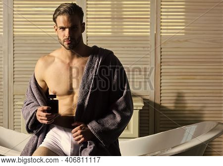 Man With Muscular Torso In Underwear And Bathrobe On Bath. Guy With Perfume Bottle In Bathroom
