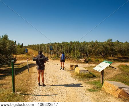 Rear View Of A Couple Of Girl Hikers With Backpacks Walking In The Path Of The Nature Park Of Strunj