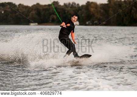 Surprised Man Holds Taut Cable In His Hands And Balances On Wave On Wakeboard