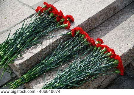 Bouquets Of Red Carnations Lie On The Old Granite Steps Of The Memorial. Memory And Patriotism. Clos
