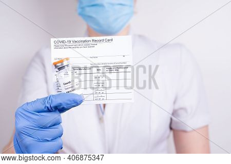 A Woman Doctor In A Mask And Gloves Holding A Vial With Covid-19 Vaccine And Vaccination Record Card