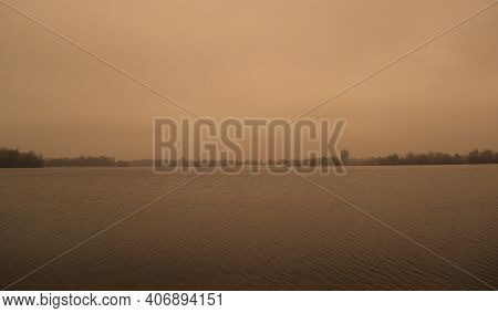 A Wide Landscape Of A Dark Gray Lake And Forest. Overcast Sky