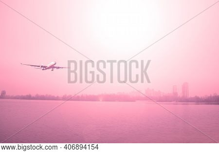 Passenger Airliner Over A Lake And A City Against A Red Sky. Air Transport
