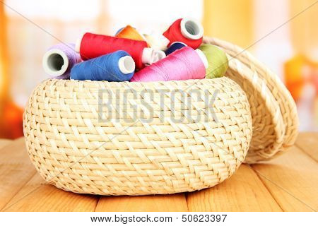 Wicker basket with accessories for needlework on wooden table, on bright background