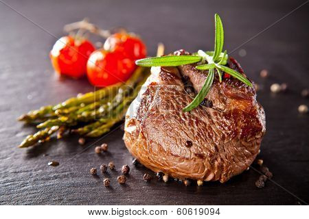 Piece of red meat steak with vegetable and herbs, served on black stone surface.