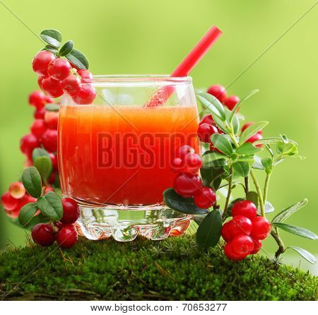 Berry juice and forest cowberry with leaves against blurred green background.