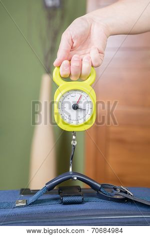 Woman checking luggage weight with a hand balance