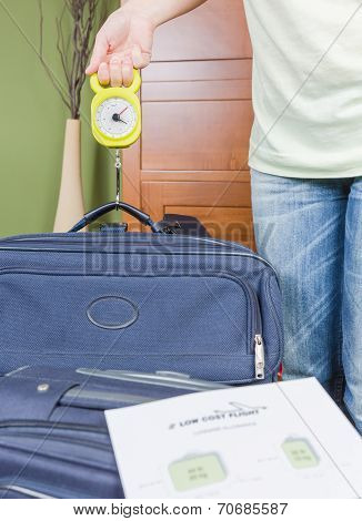 Woman checking luggage weight with a hand balance