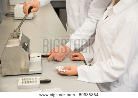 Team of pharmacists using press to make pills at the laboratory