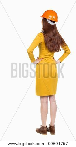 Backview of an woman engineer in construction helmet stands. Standing young woman. Rear view people collection.  backside view of person.  I Confident woman in a helmet stands with hands on waist.