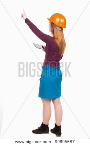Backview of business woman in construction helmet with  tablet pc pointing. Standing young girl. Rear view people collection.  backside view of person. Engineer scorekeeper hand shows the work front.