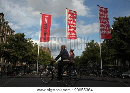 AMSTERDAM, NETHERLANDS - AUGUST 9, 2012: Two cyclists pass over the bridge decorated with banners with an official brand of the city in Amsterdam, Netherlands.