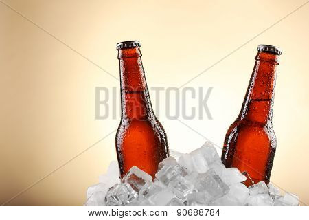 Glass bottles of beer in ice cubes on color background