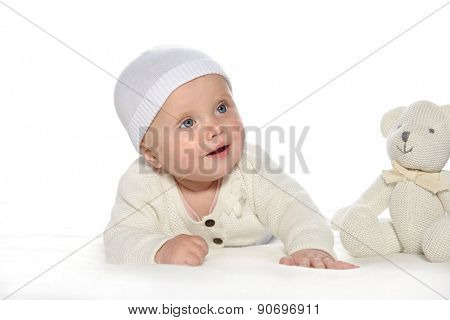 baby girl child lying down on white blanket smiling happy white  hat warm cloting fashion portrait face studio shot isolated on white caucasian teddy bear