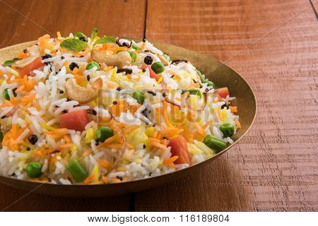 Veg biryani or veg pulav served in a round brass bowl over wooden background