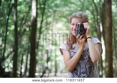 Young girl in casual clothes with old retro vintage camera photographing in forest. Brown hair, long