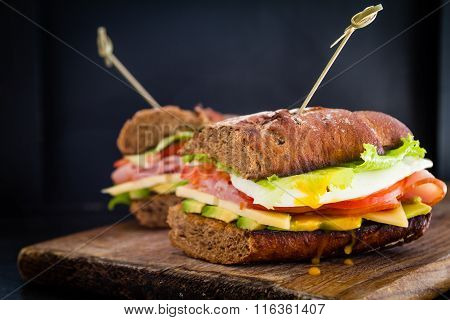 Large sandwich with avocado ham chese and egg, dark background